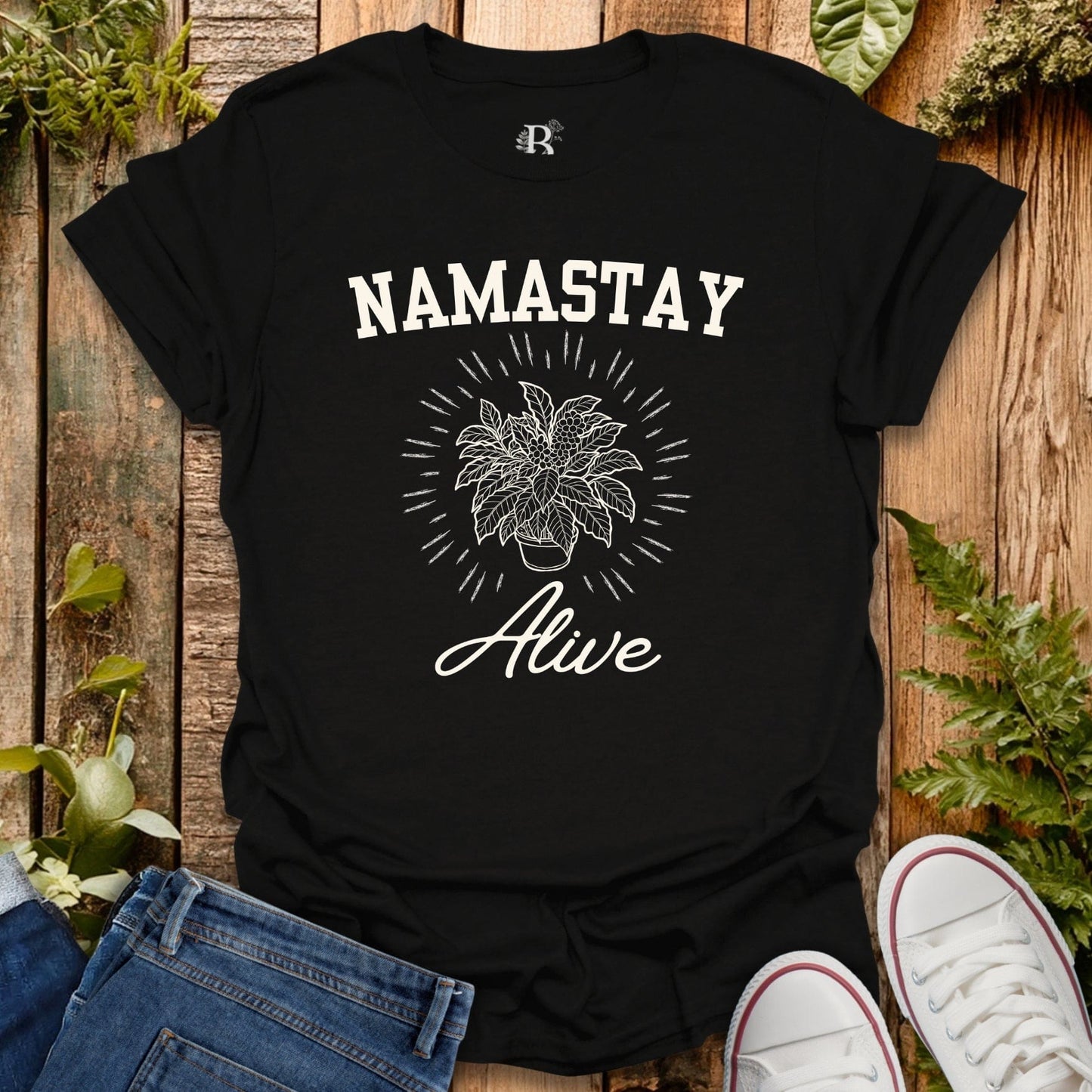 Black t-shirt with 'Namastay Alive' design on a wooden surface with plants.