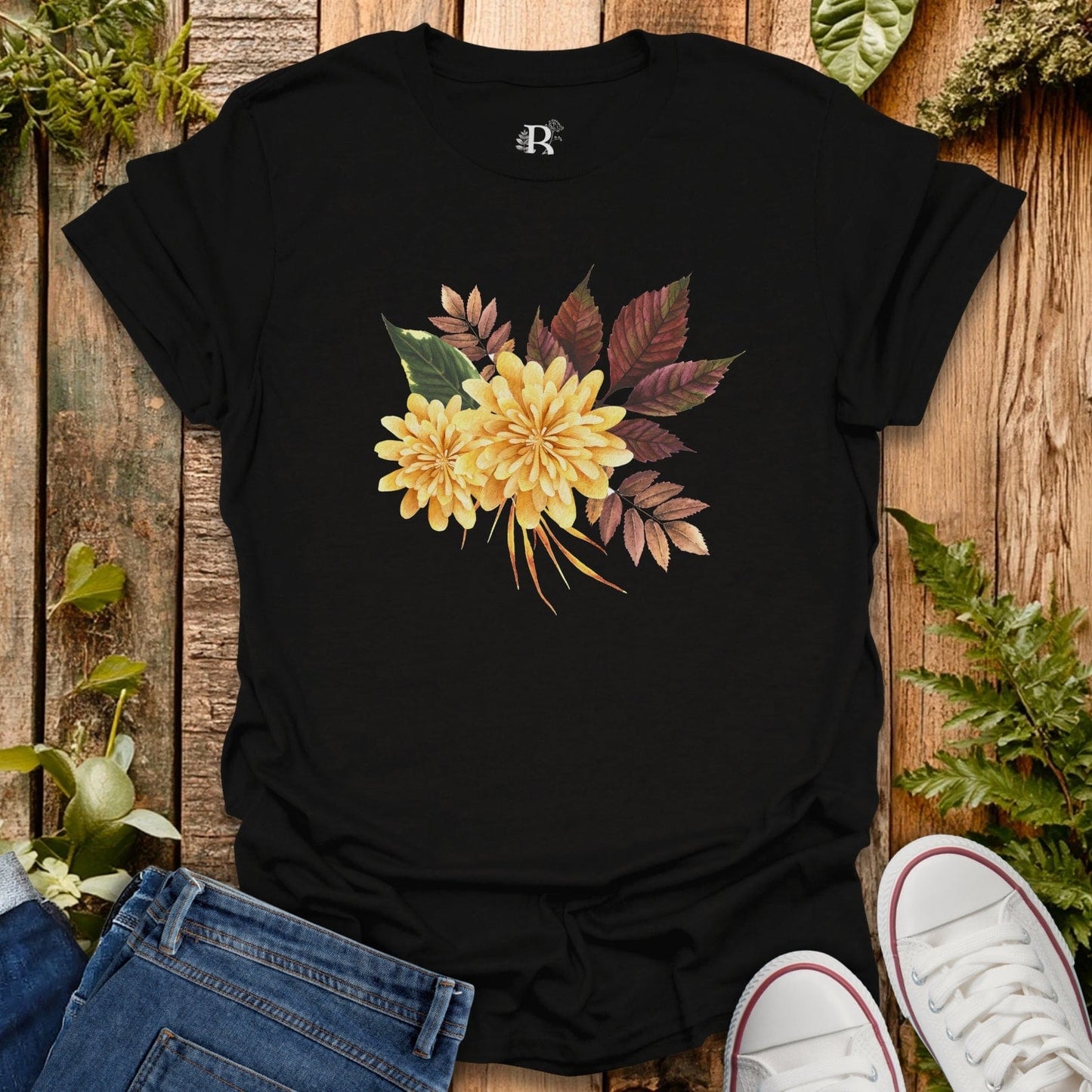 Black t-shirt with yellow floral design on a wooden surface with plants.