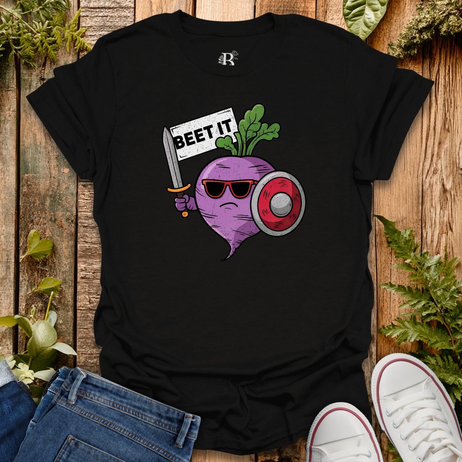 Black t-shirt with a graphic design of a beet holding a sword and sunglasses, surrounded by plants on a wooden surface.