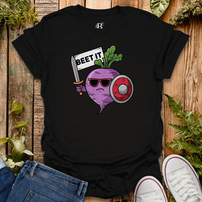 Black t-shirt with a graphic design of a beet holding a sword and sunglasses, surrounded by plants on a wooden surface.