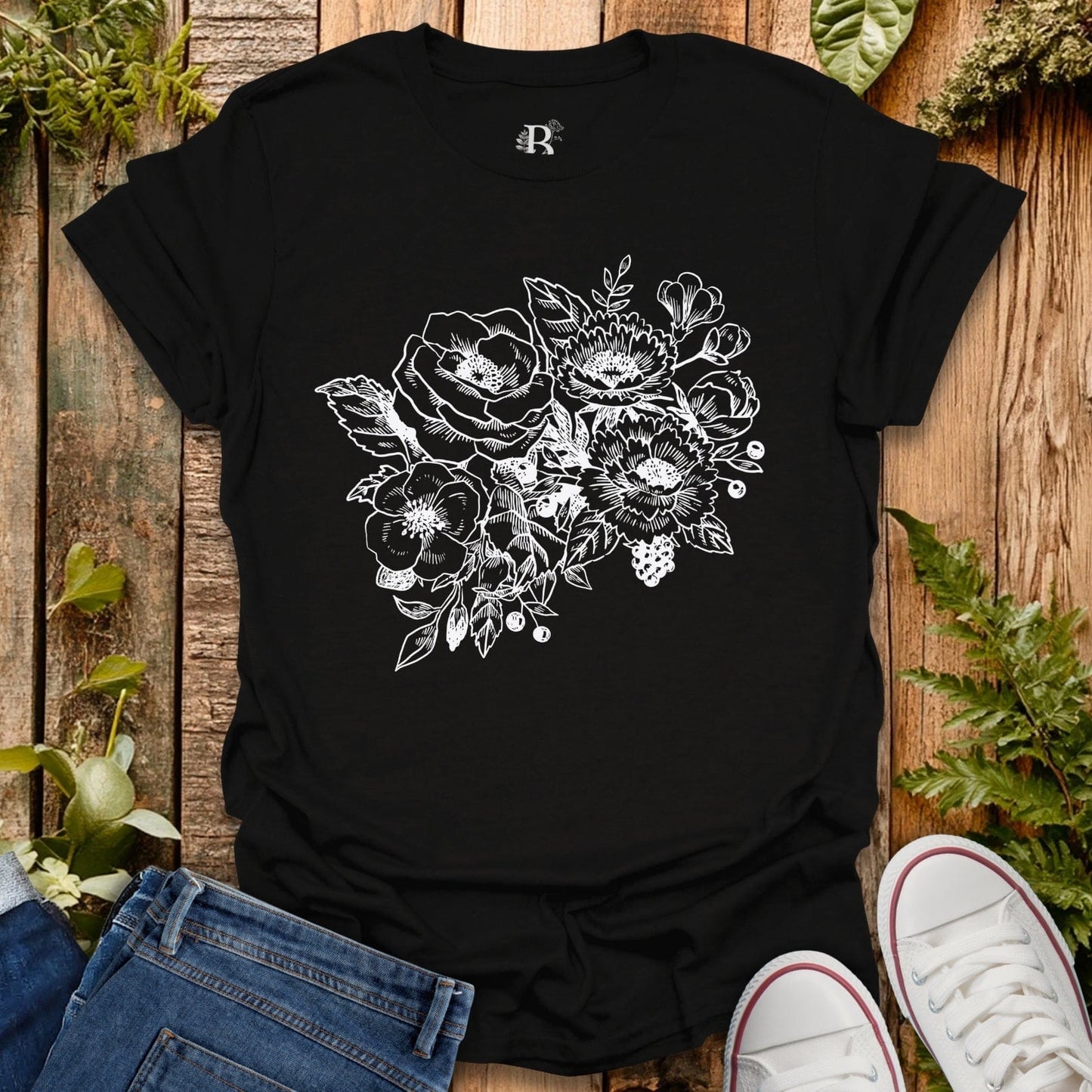 Black t-shirt with floral design on a wooden surface with jeans and sneakers.