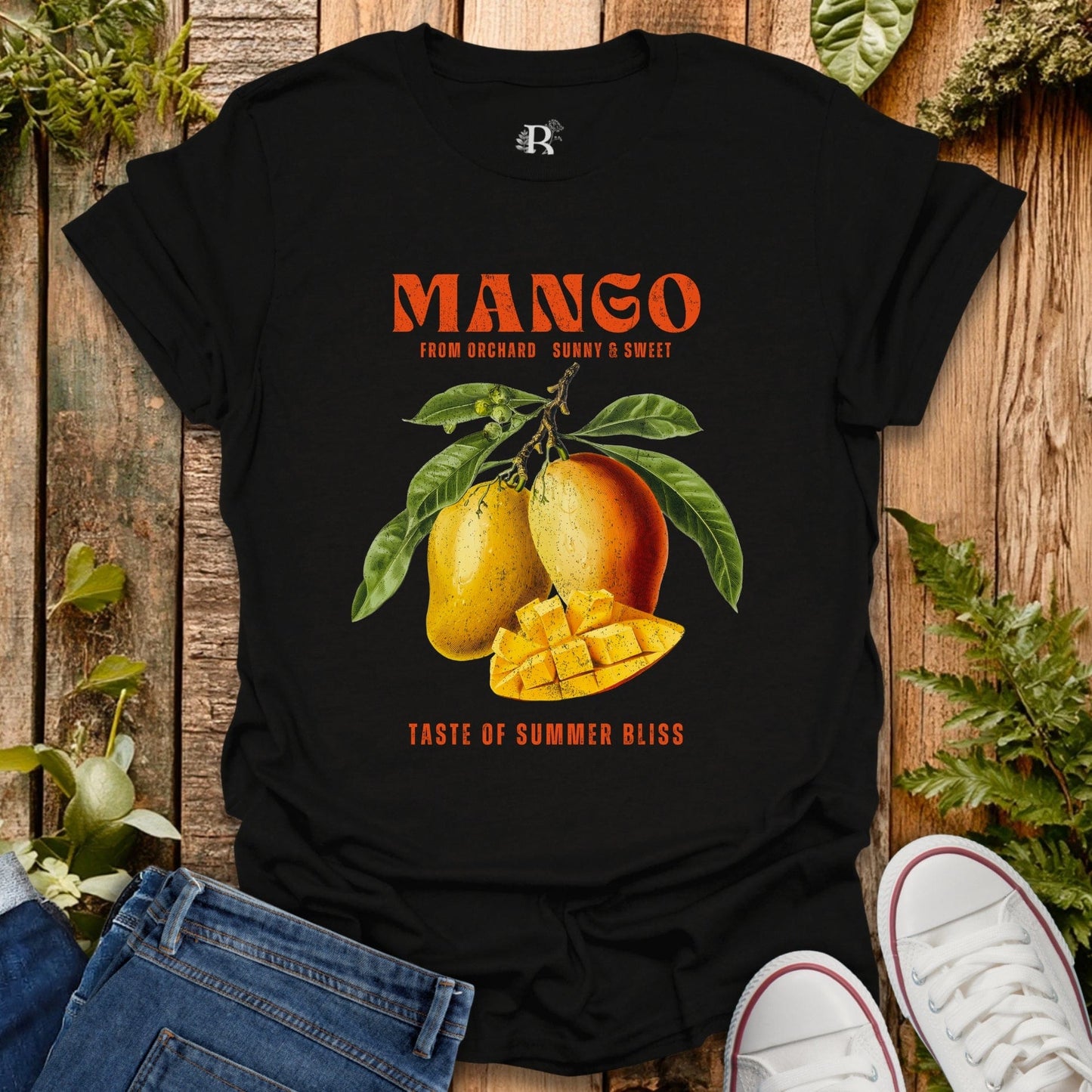 Black t-shirt with mango graphic and text on a wooden surface with plants.