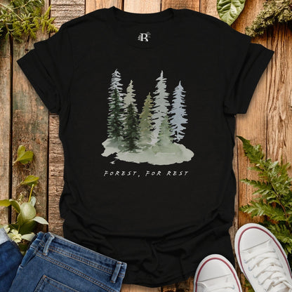Black t-shirt with forest graphic and text on a wooden surface with plants.