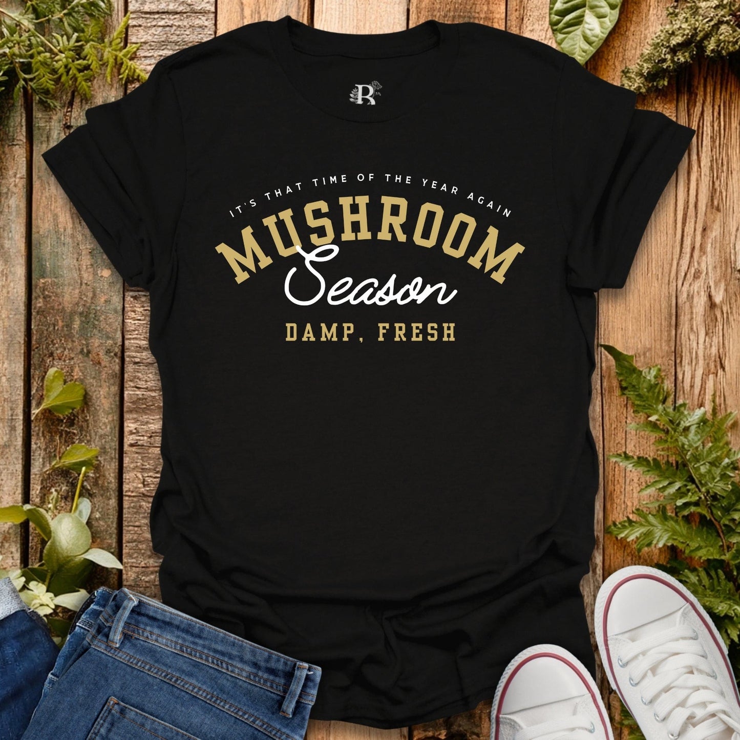 Black t-shirt with 'Mushroom Season' text on a wooden surface with plants.