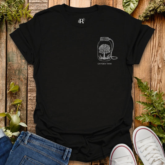 Black t-shirt with a design of an oxygen tank and tree, placed on a wooden surface with plants around.