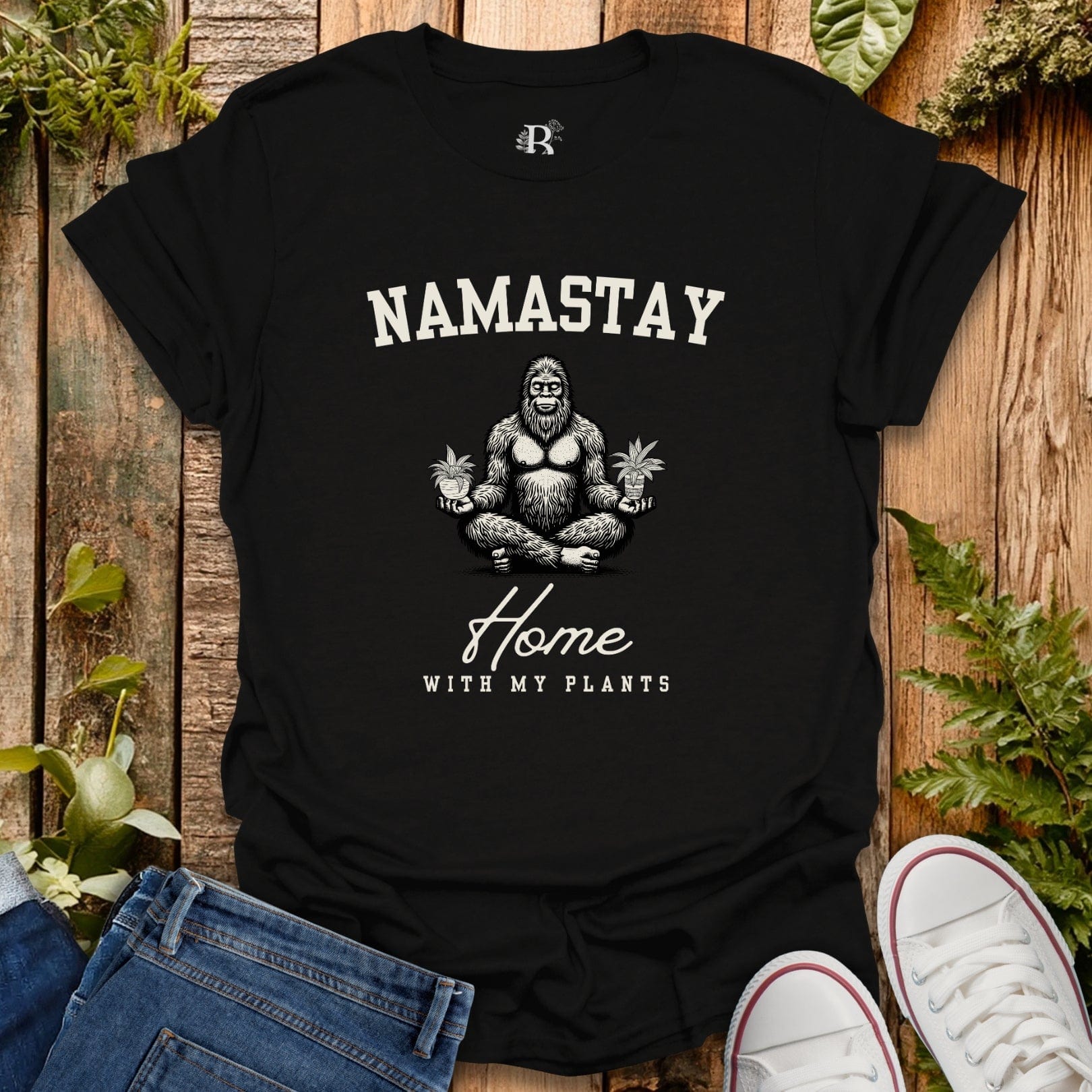 Black t-shirt with 'Namastay Home with My Plants' design on a wooden surface with plants.