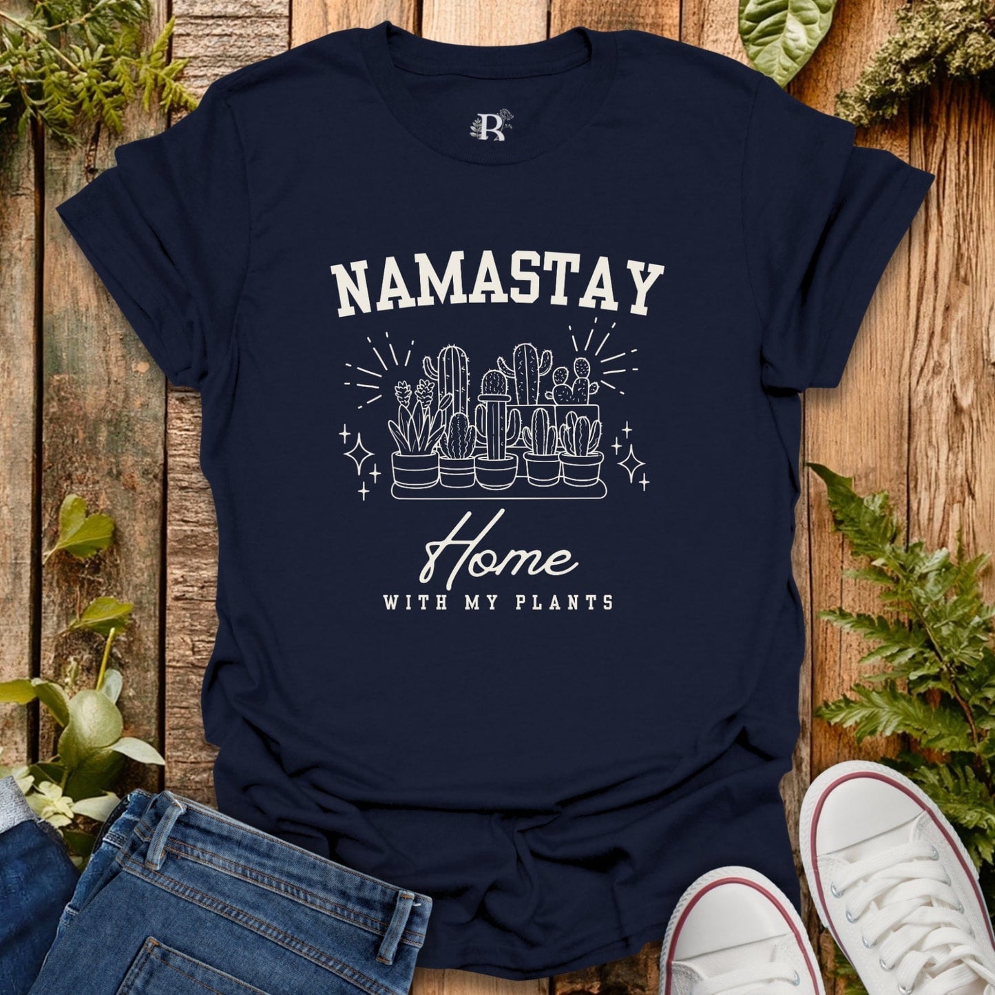Navy blue t-shirt with 'Namastay Home with My Plants' design on a wooden surface with plants.