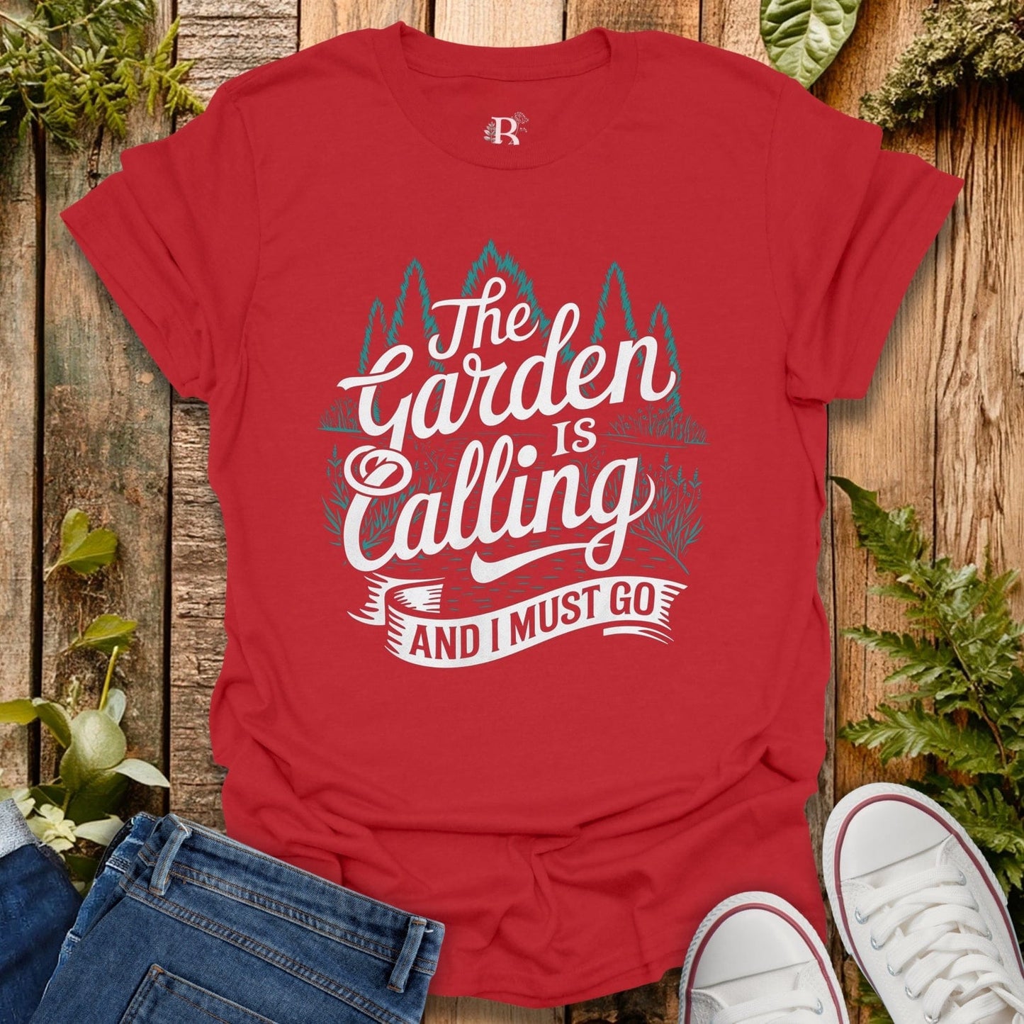 Red t-shirt with 'The Garden is Calling and I Must Go' text on a wooden background with plants.