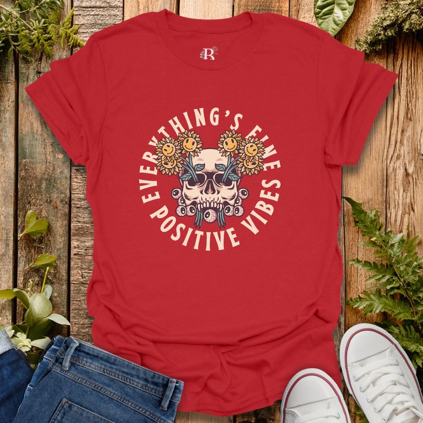 Red t-shirt with skull and floral design on a wooden surface with jeans and sneakers.