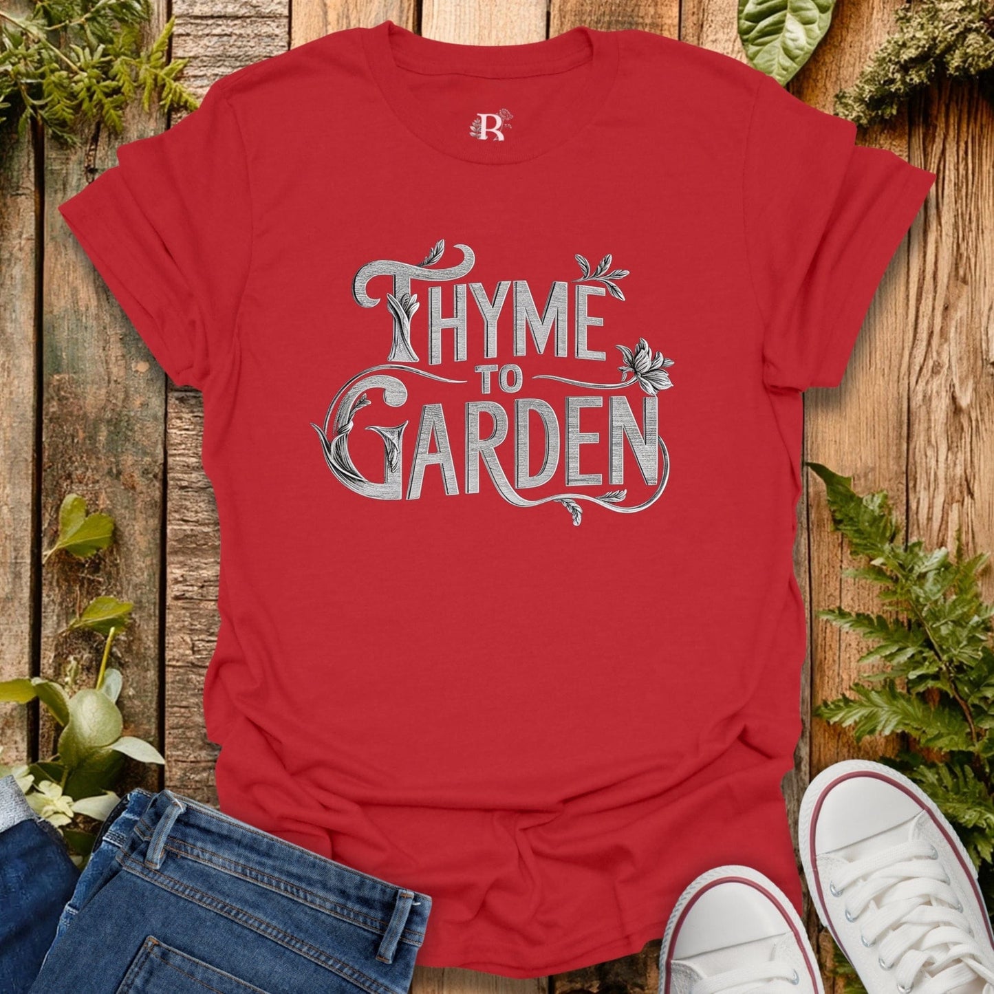 Red t-shirt with 'Thyme to Garden' text on a wooden background with plants.