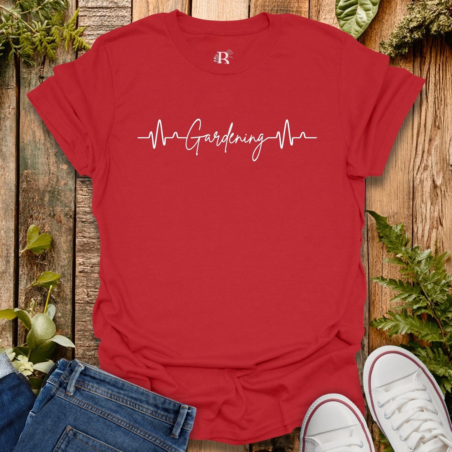 Red t-shirt with 'Gardening Heartbeat' design on a wooden surface with plants.
