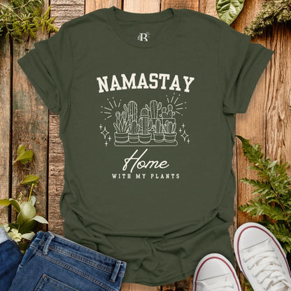 Green t-shirt with 'Namastay Home with My Plants' design on a wooden background with plants.