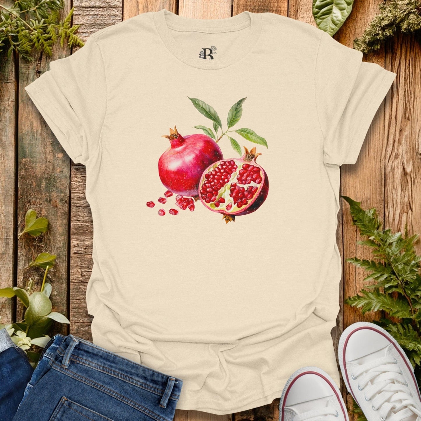 Beige t-shirt with pomegranate design on a wooden surface with plants.