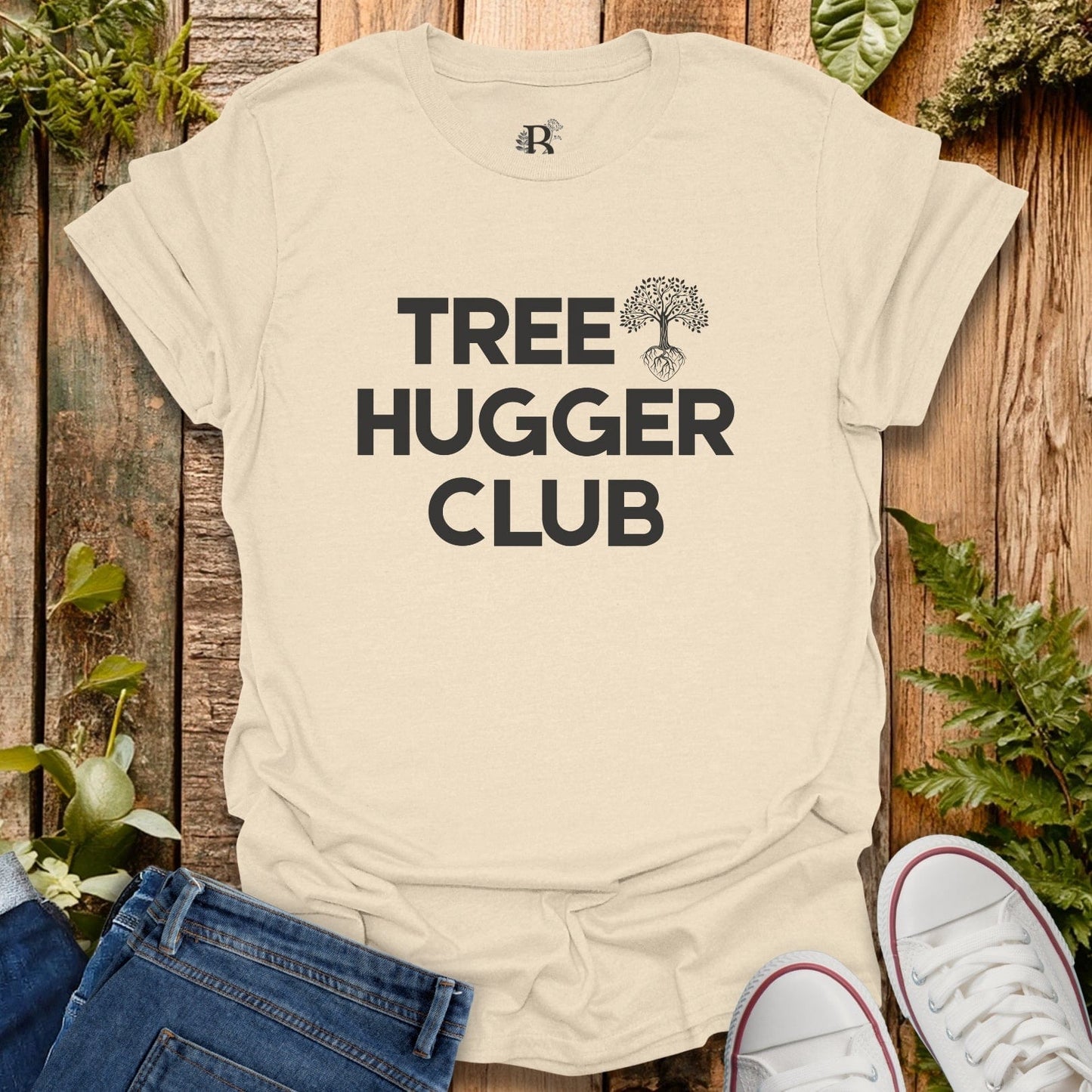 Beige t-shirt with 'Tree Hugger Club' text on a wooden background with plants.