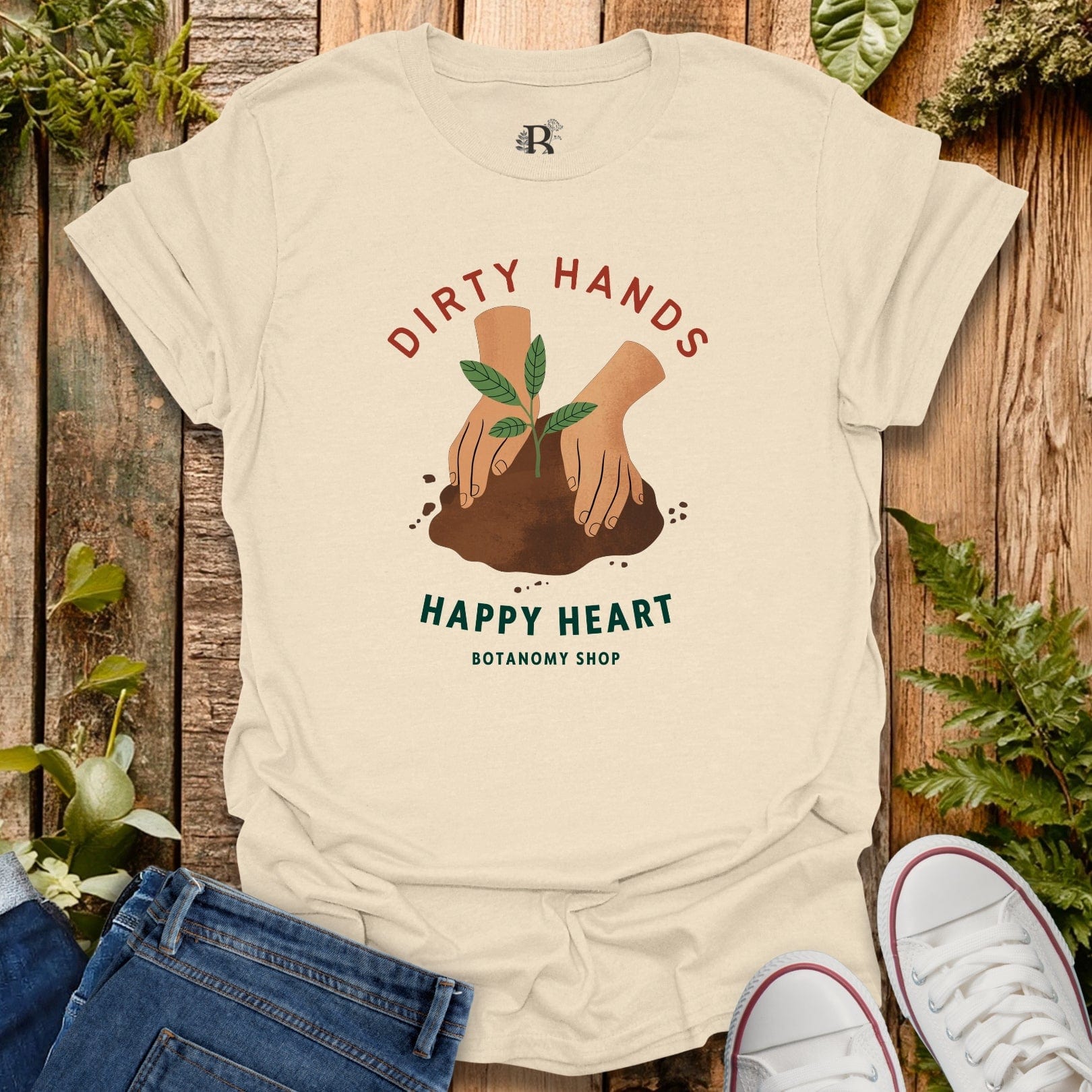 Beige t-shirt with 'Dirty Hands Happy Heart' graphic on a wooden background with plants.