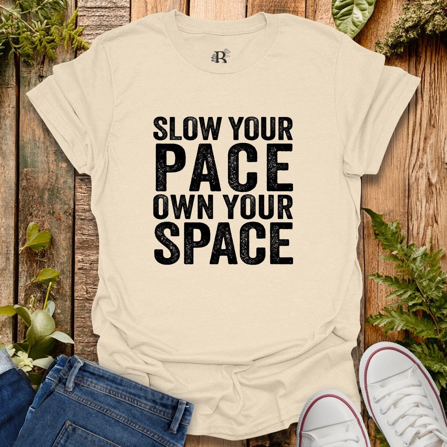 Beige t-shirt with 'Slow your pace, own your space' text on a wooden background