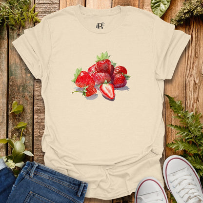 Beige t-shirt with strawberry design on a wooden surface with plants.
