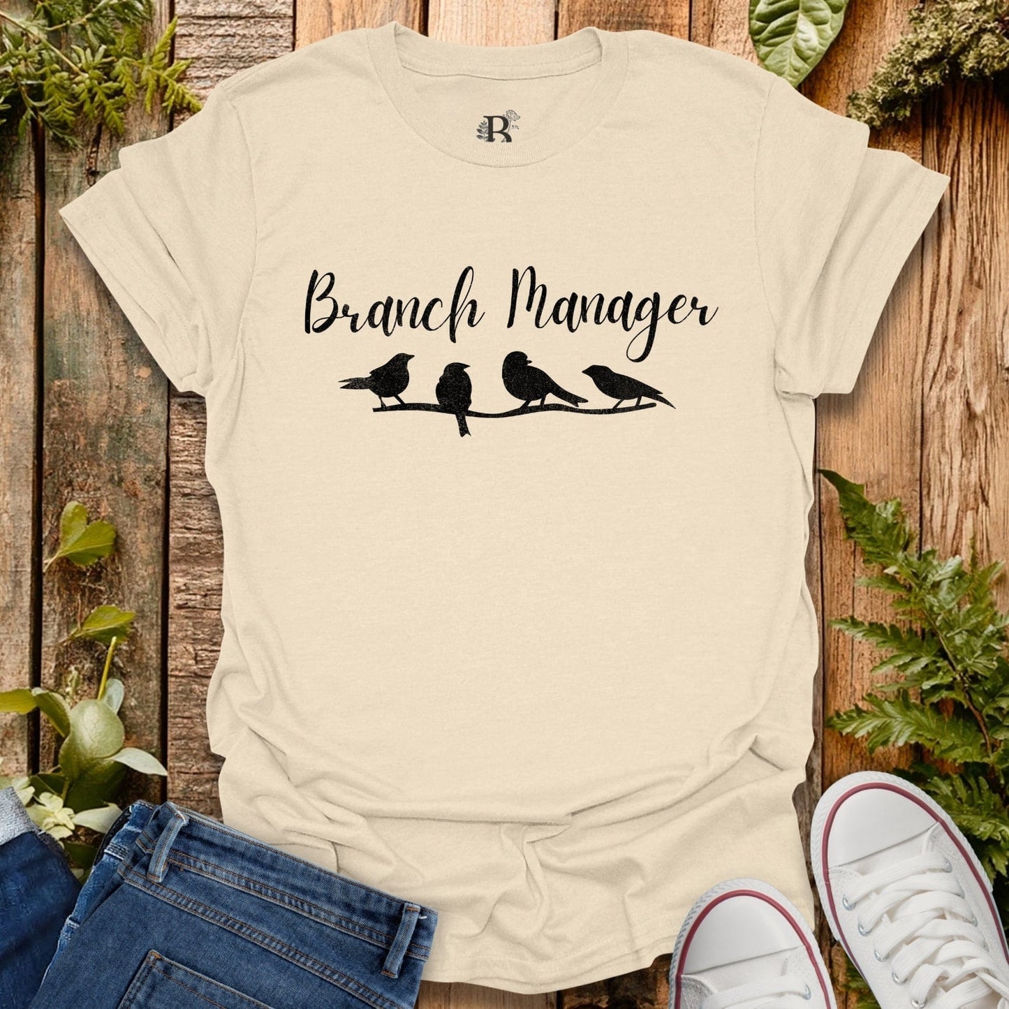 Beige t-shirt with 'Branch Manager' and bird design on a wooden background