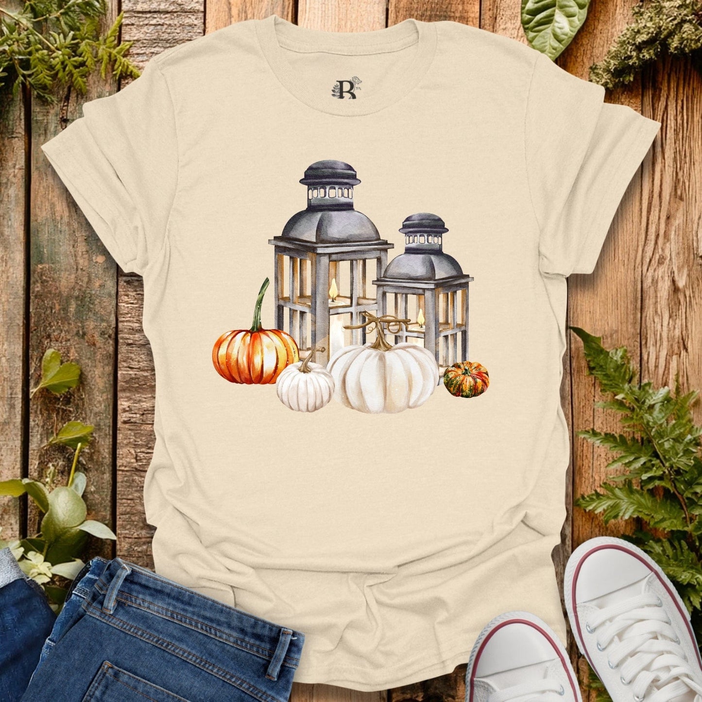 Beige t-shirt with lantern and pumpkin design on a wooden background