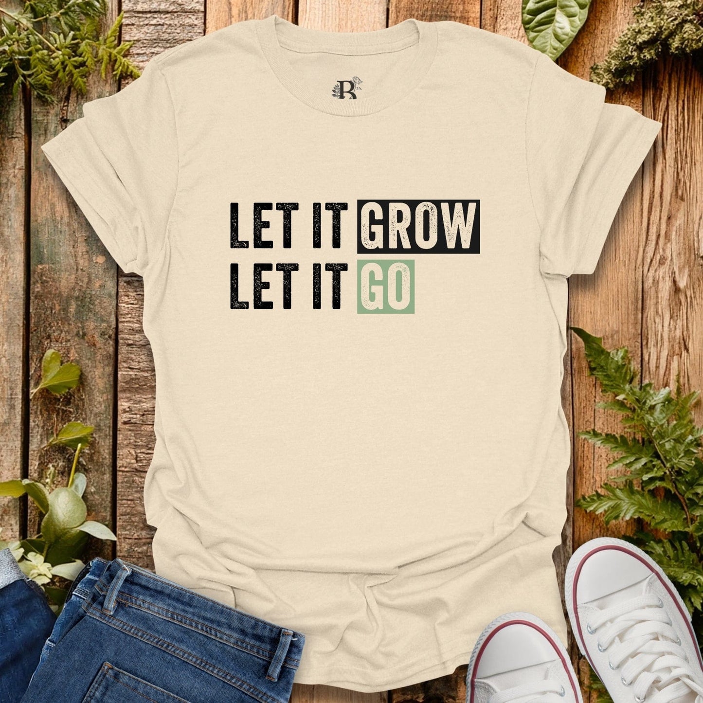 Beige t-shirt with 'LET IT GROW LET IT GO' text on a wooden background with plants.