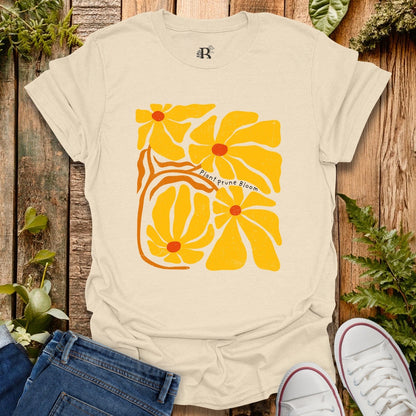 Beige t-shirt with yellow floral design on a wooden surface with plants.