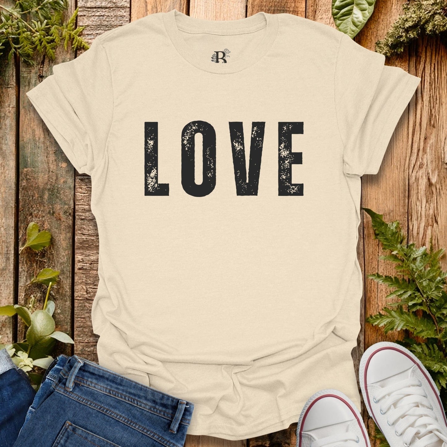 Beige t-shirt with 'LOVE' printed on it, displayed against a wooden background with plants.