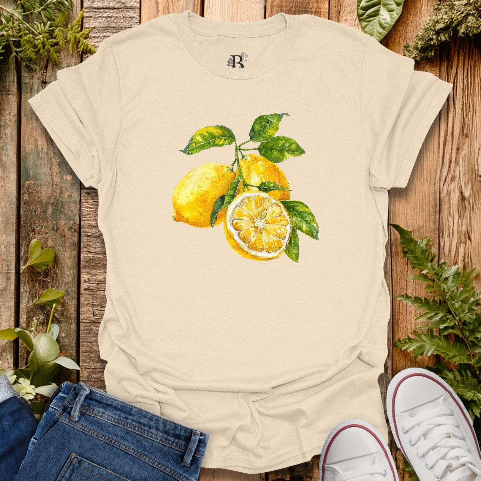 Beige t-shirt with lemon design on a wooden surface with plants.