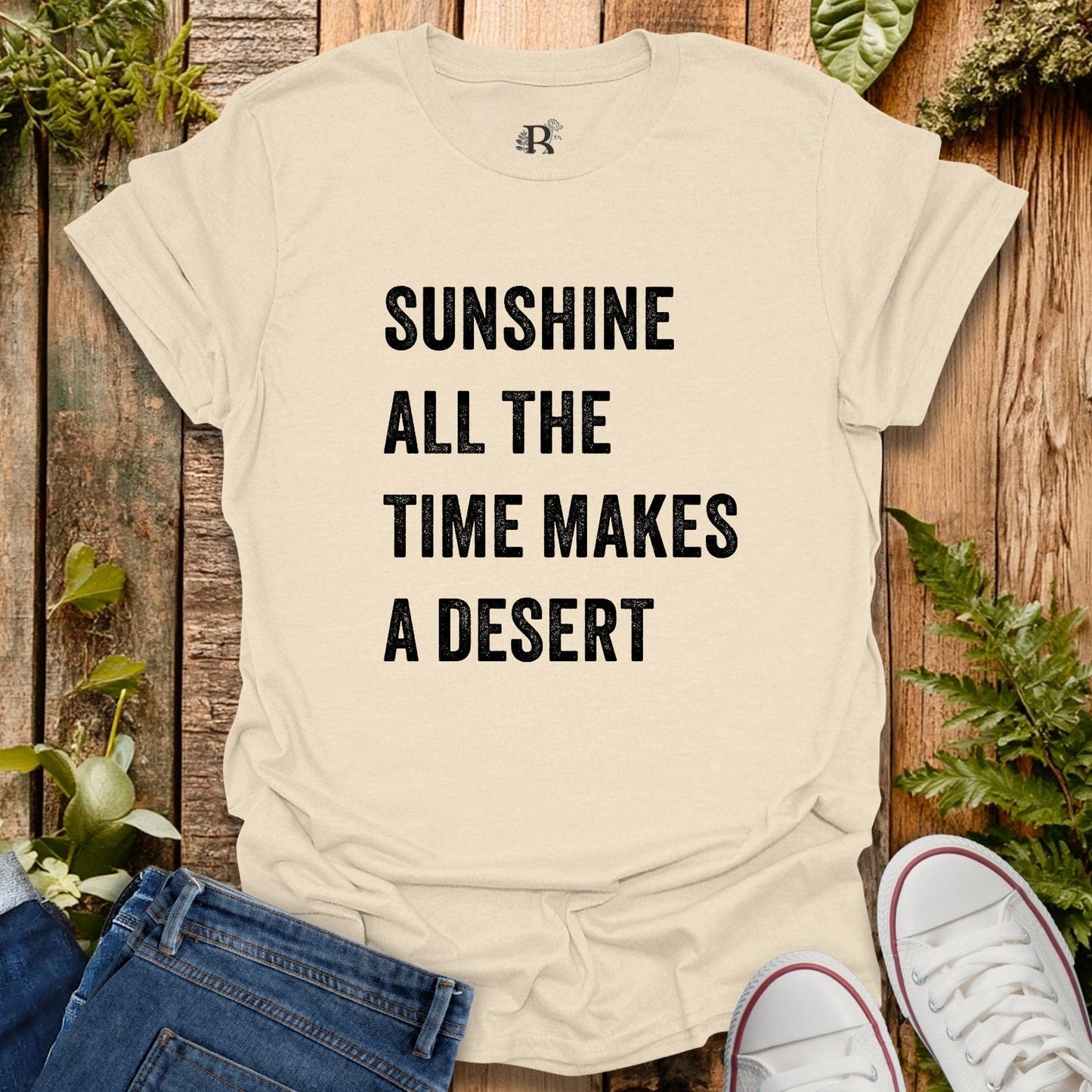 Beige t-shirt with text 'Sunshine all the time makes a desert' on a wooden background with plants.