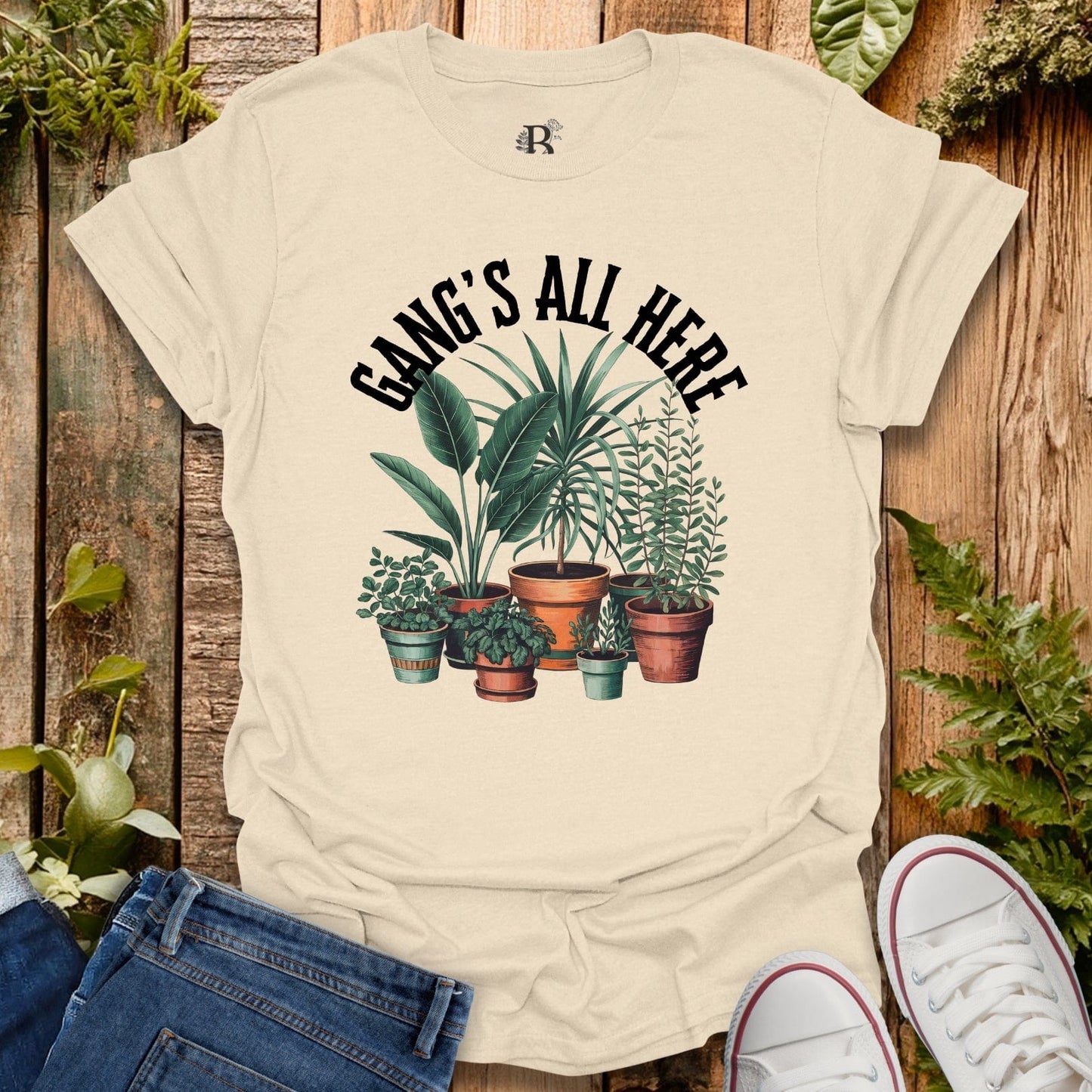 Beige t-shirt with plant design and 'Gang's All Here' text on a wooden background
