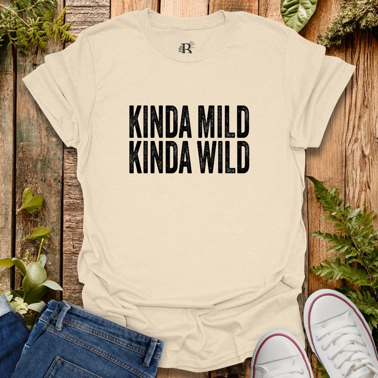 Beige t-shirt with 'KINDA MILD KINDA WILD' text on a wooden background with plants.