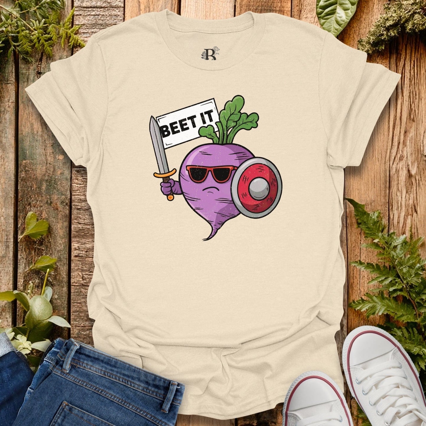 Beige t-shirt with a graphic of a beet holding a sword and sign, 'BEET IT', on a wooden background.