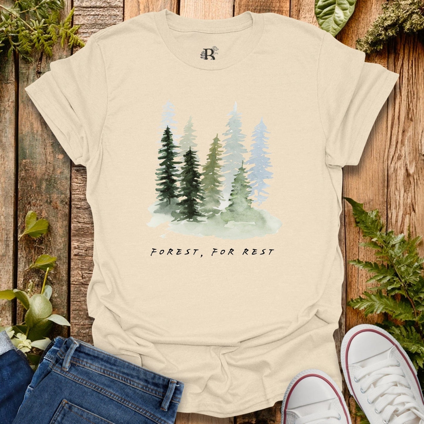 Beige t-shirt with forest graphic and text 'Forest, For Rest' on a wooden background