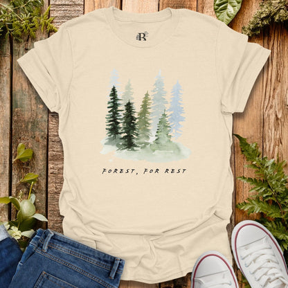 Beige t-shirt with forest graphic and text 'Forest, For Rest' on a wooden background