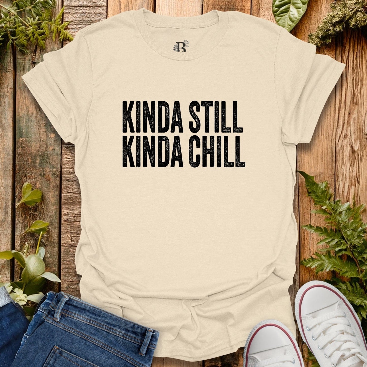 Beige t-shirt with 'Kinda Still Kinda Chill' text on a wooden background