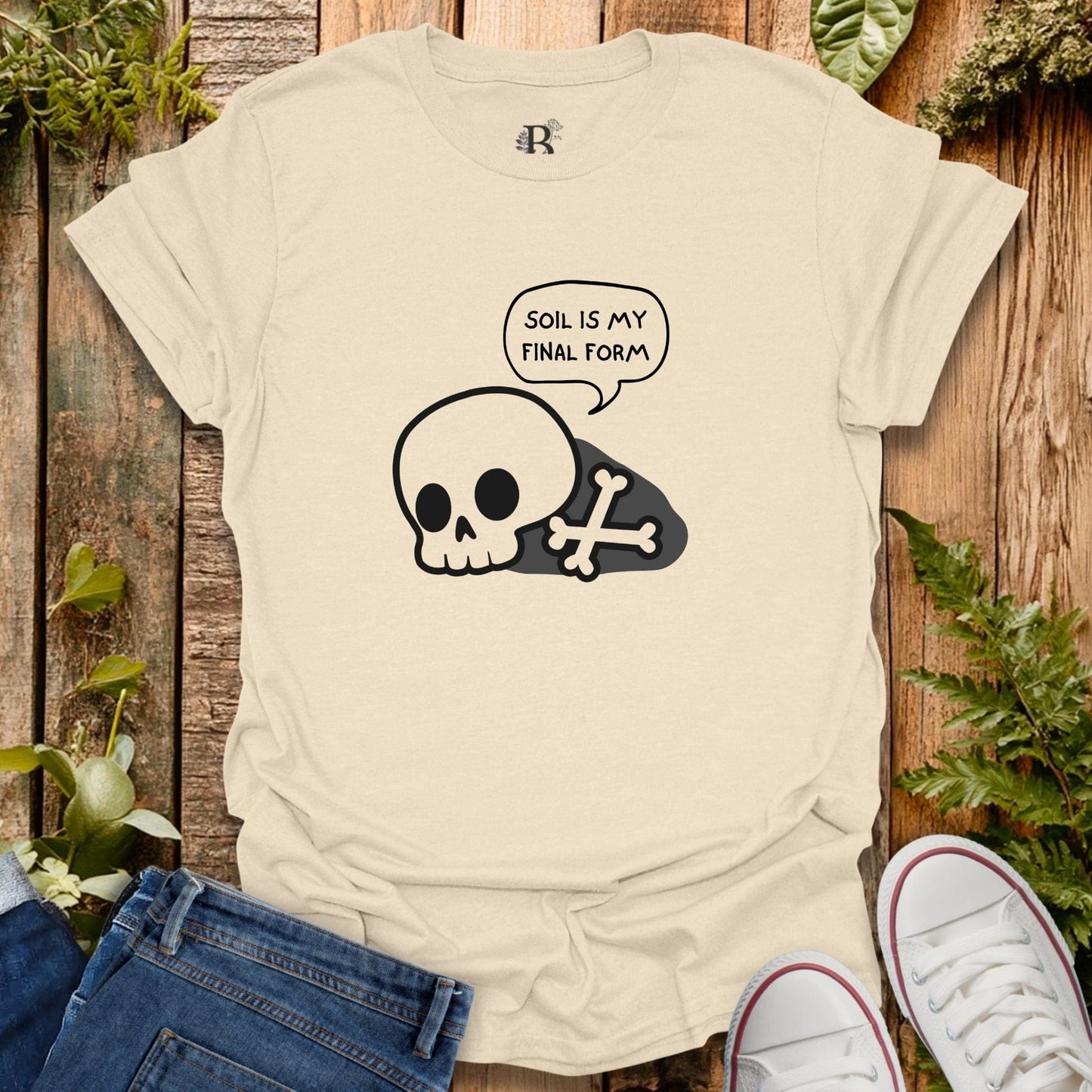 Beige t-shirt with skull and bone graphic and 'Soil is my final form' text on a wooden background.