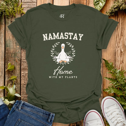 Green t-shirt with 'Namastay Home with My Plants' design on a wooden background with plants.