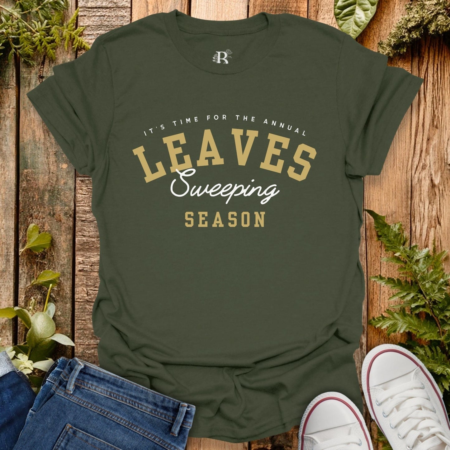 Green t-shirt with 'Leaves Sweeping Season' text on a wooden background with leaves.