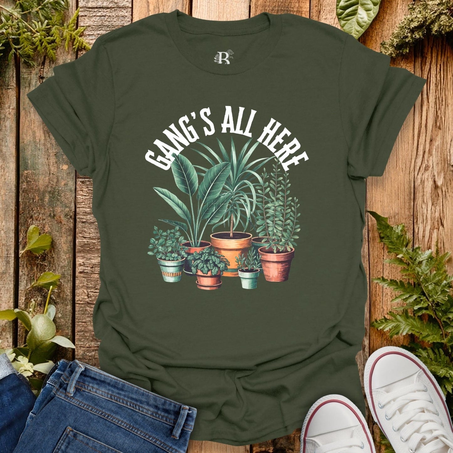 Green t-shirt with plant design and text 'Gang's All Here' on a wooden background