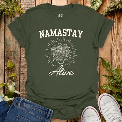 Green t-shirt with 'Namastay Alive' design on a wooden background with plants.