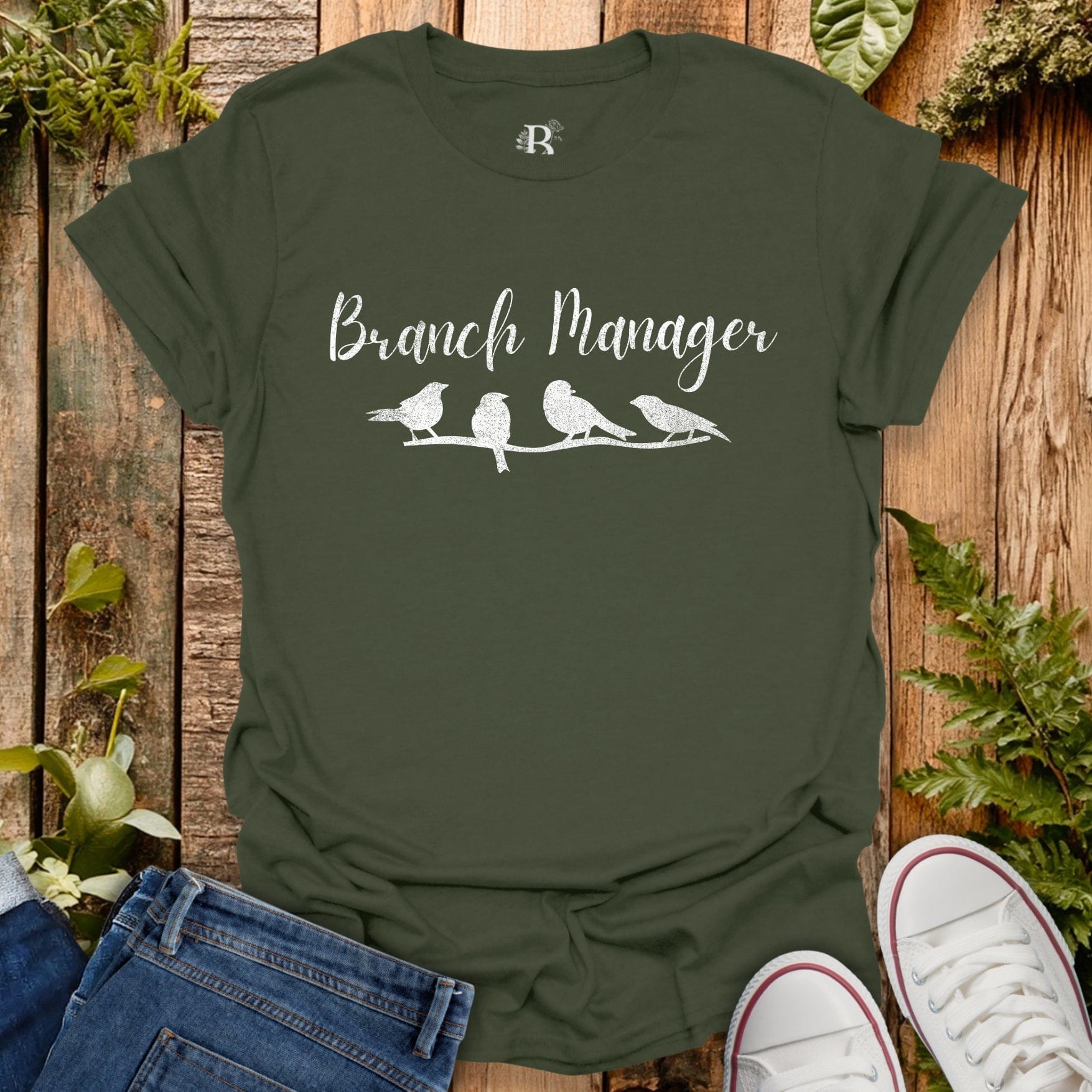 Green t-shirt with 'Branch Manager' text and bird illustrations on a wooden background