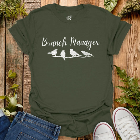 Green t-shirt with 'Branch Manager' text and bird illustrations on a wooden background
