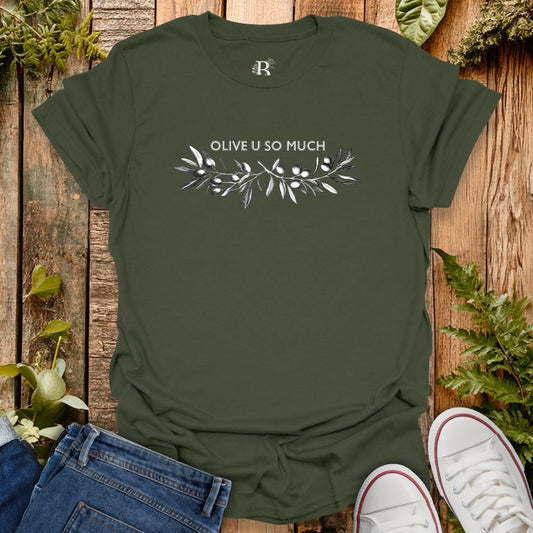 Green t-shirt with 'OLIVE U SO MUCH' text and leaf design on a wooden background with plants.
