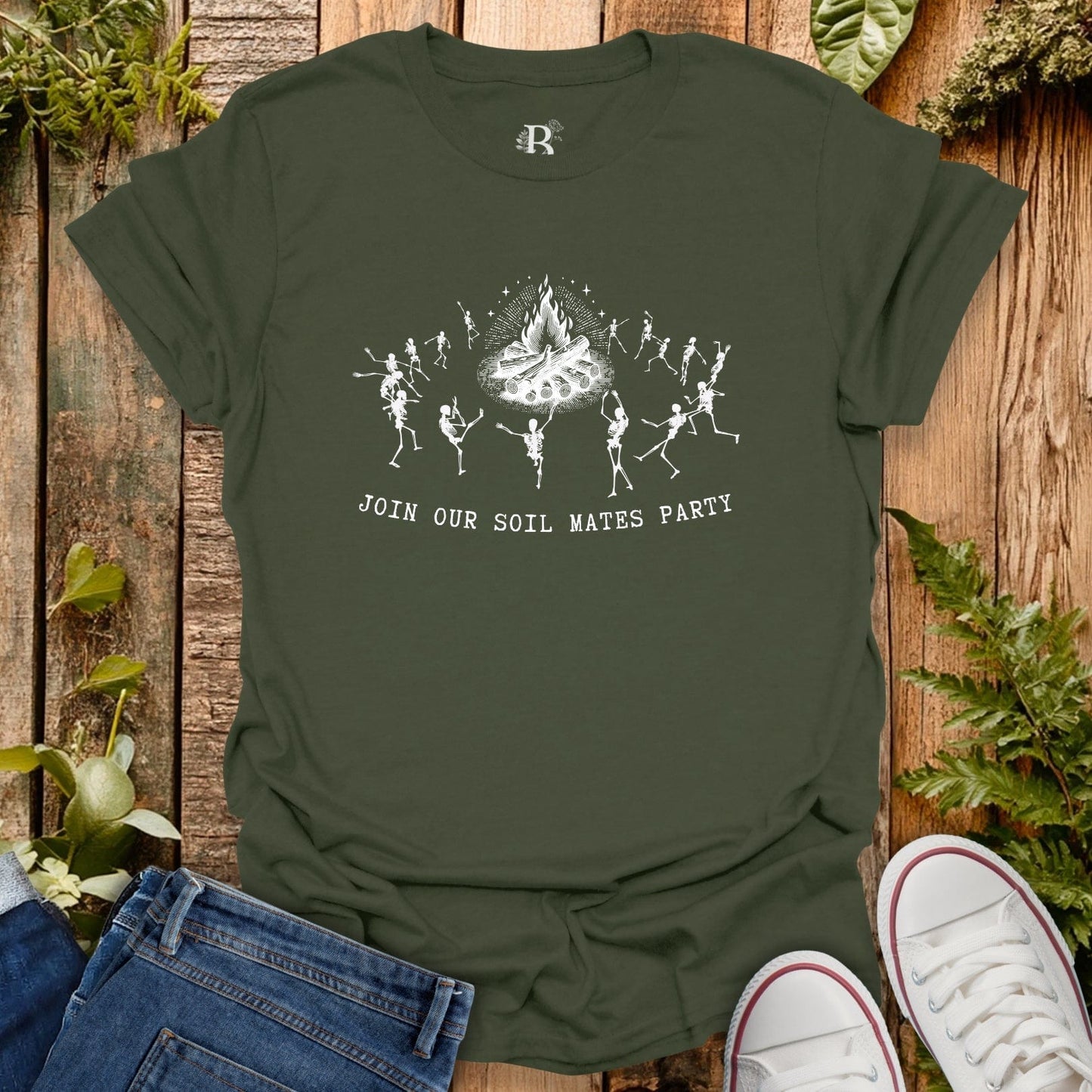 Green t-shirt with skeleton design and text on a wooden surface with plants.