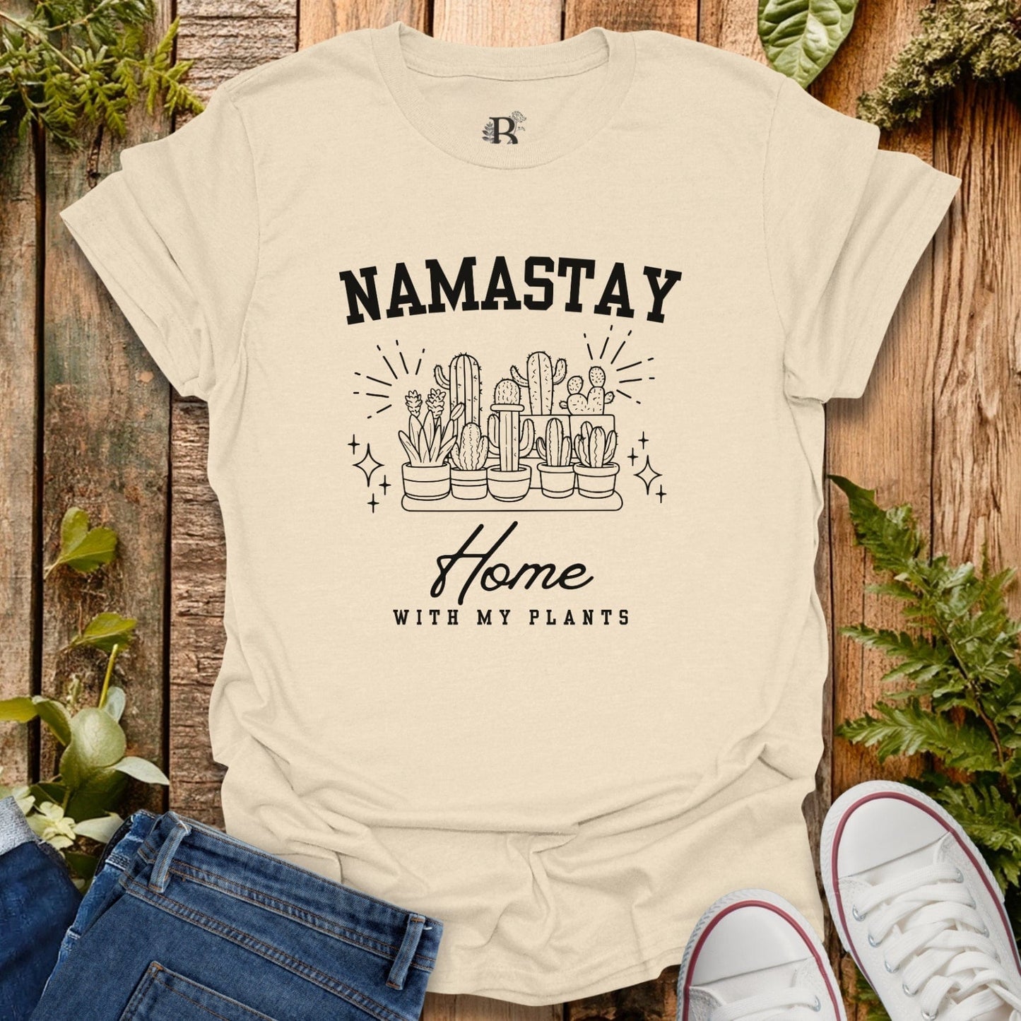 Beige t-shirt with 'Namastay Home with My Plants' design on a wooden background with plants.
