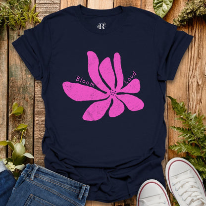 Navy blue t-shirt with pink flower graphic and text on a wooden surface with plants.