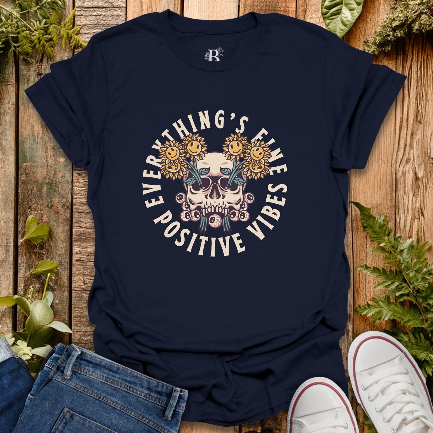Navy blue t-shirt with skull and sunflower design on a wooden surface with jeans and sneakers.