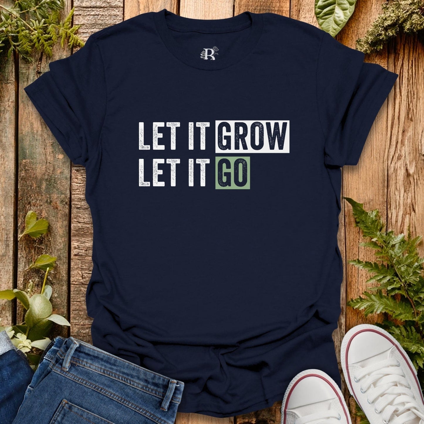 Navy blue t-shirt with 'LET IT GROW LET IT GO' text on a wooden surface with plants.