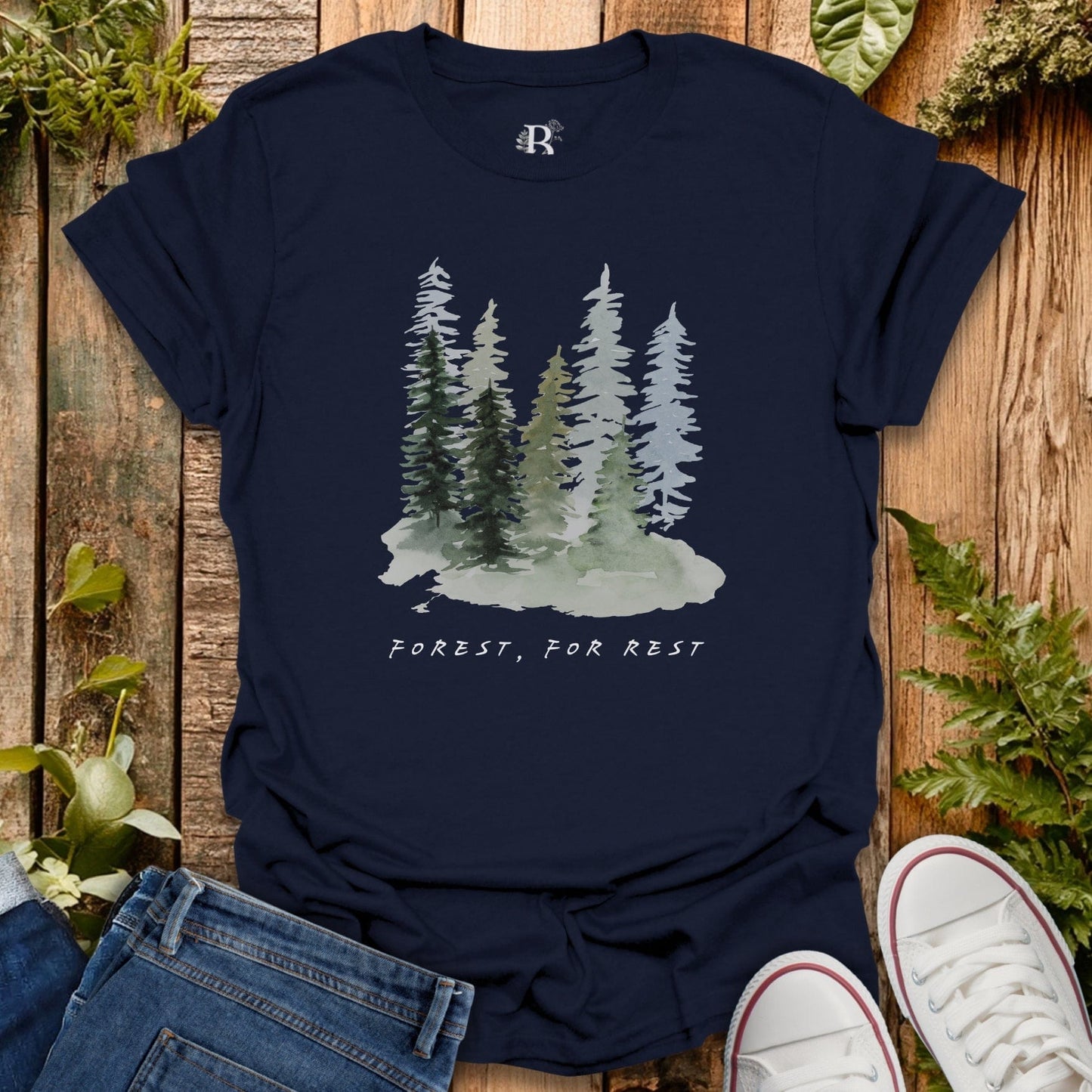 Navy blue t-shirt with forest graphic and 'Forest, For Rest' text on a wooden surface with plants.