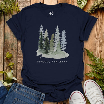 Navy blue t-shirt with forest graphic and 'Forest, For Rest' text on a wooden surface with plants.