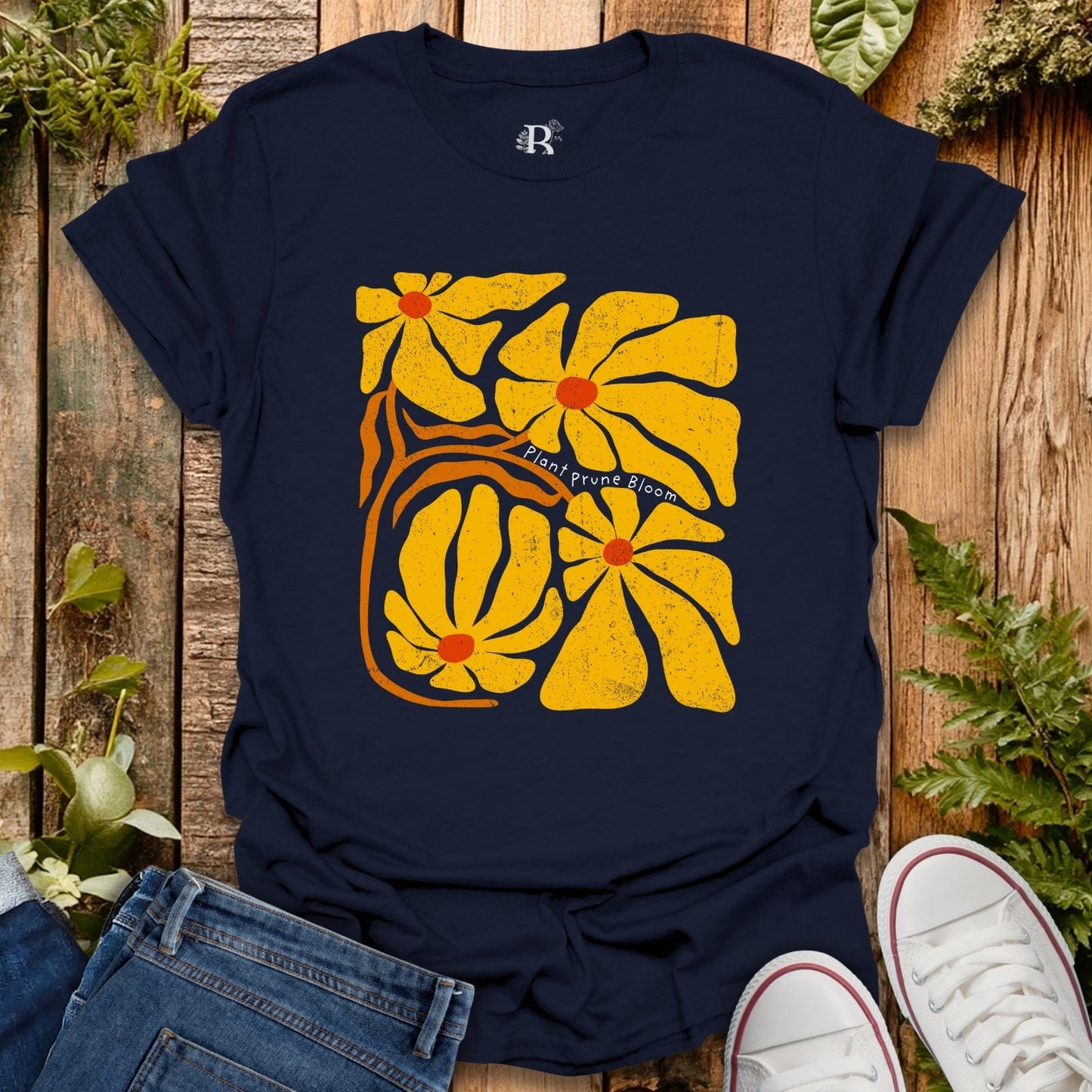 Navy blue t-shirt with yellow floral design on a wooden surface with plants.
